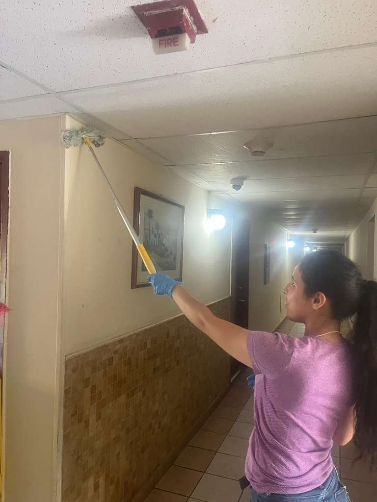 Crew member dusting high surfaces in a hallway